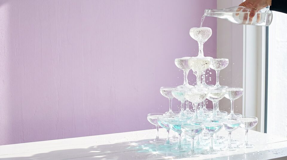 Sparkling water poured into the top glass of a coupe tower spills down and fills every glass below.